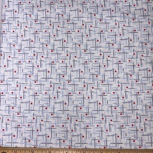 May include: A white fabric featuring a repeating geometric pattern of small dark blue and light blue dotted lines forming cross shapes, interspersed with tiny red stars. A wooden ruler is placed at the bottom, showing an 8-inch measurement.
