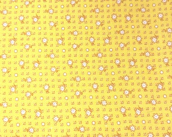 May include: A bright yellow fabric featuring a repeating pattern of small white flowers with orange centers and tiny white dots. A wooden ruler is positioned at the bottom, showing measurements in inches from 3 to 8 inches across the fabric.