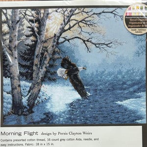 May include: A Dimensions counted cross stitch kit titled Morning Flight by Persis Clayton Weirs. The package features a bald eagle flying over a snowy landscape with birch trees. It includes presorted cotton thread, 16 count grey Aida, a needle, and instructions for an 18 inch by 15 inch fabric.