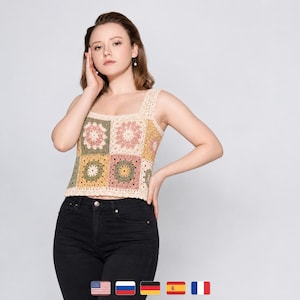 May include: A square-patterned crochet top in cream, pink, green, and yellow. The top has a square neckline and wide straps. The model is wearing black jeans.