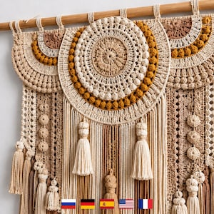 May include: A large, handcrafted macrame wall hanging in shades of beige, cream, and mustard yellow. The design features circular and semi-circular crochet patterns, tassels, and fringe. The wall hanging is suspended from a wooden rod.