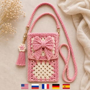 May include: A rectangular crochet crossbody bag featuring a pink and cream granny square pattern. The bag has a flap adorned with a large pink crocheted bow and a long pink strap. A pink flower charm with a tassel hangs from a gold metal clasp.