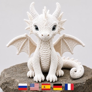 Può includere: Figurina di drago all'uncinetto bianco sporco, con dettagli intricati su ali, corna e coda. Il drago ha grandi occhi ed è seduto su una pietra. Un affascinante pezzo decorativo fatto a mano.