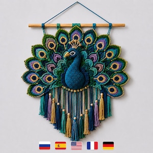 May include: A crocheted peacock wall hanging featuring a dark blue body and a large, fanned tail with intricate green, blue, and purple feather patterns. The piece is suspended from a wooden dowel with hanging yarn tassels and wooden beads.