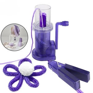 Può includere: Una macchina per maglieria in plastica viola con manovella, un cilindro superiore trasparente e un filo di lana viola. Include una clip di tensione in plastica viola e una forma di fiore lavorata a maglia viola con un pompon bianco.
