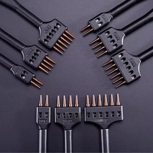 May include: A set of black leather stitching chisels with copper-colored prongs. The tools feature varying numbers of prongs, including two, four, and six-prong configurations, each with a black handle and clearly marked numerical indicators.