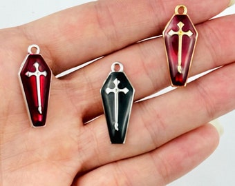 May include: Three coffin-shaped charms with a cross design. One charm is black with a white cross, another is red with a silver frame and cross, and the third is red with a gold frame and cross. These charms are ideal for jewelry making.