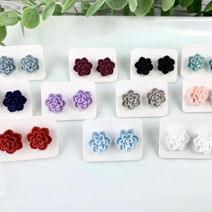 May include: Assortment of 12 pairs of small flower-shaped stud earrings in various colors, including red, blue, purple, white, and gray. The earrings are displayed on white cards.