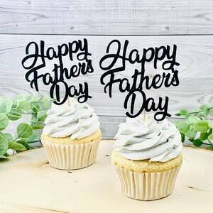 Può includere: Due cupcake con glassa bianca sormontati da topper per cupcake con glitter nero che recitano "Happy Father's Day".