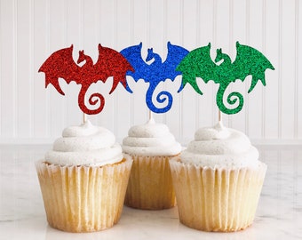 May include: Three cupcakes decorated with glitter dragon toppers. The dragons are red, blue, and green.