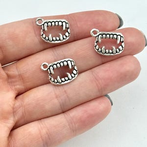 May include: Three silver charm pendants shaped like a set of teeth. The charms are detailed with sharp points and a rounded edge.