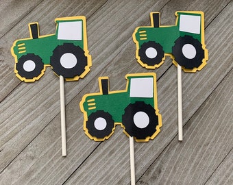 May include: Three green and yellow tractor cupcake toppers. Each topper has a white circle for a wheel and a yellow rectangle for a window.