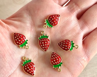 Puede incluir: Seis abalorios de fresa de tono dorado con esmalte rojo y hojas verdes. Cada abalorio tiene un anillo de salto para sujetarlo a joyas u otras manualidades.