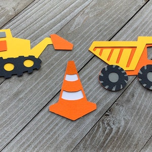 May include: A set of three construction vehicle paper cutouts. The set includes a yellow excavator, a yellow dump truck, and an orange traffic cone.