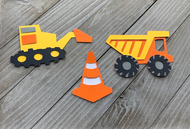 May include: A set of three construction vehicle paper cutouts. The set includes a yellow excavator, a yellow dump truck, and an orange traffic cone.