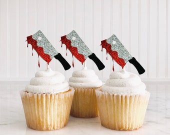 Può includere: Tre cupcake sormontati da decorazioni a forma di coltello con glitter argentati e rossi. I coltelli sono a forma di coltelli da macellaio con glitter rossi che gocciolano sui lati.