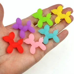 May include: Seven balloon dog charms in various colors, including red, pink, purple, light blue, green, and yellow. The charms are made of a translucent, rubber-like material and are shaped like balloon animals.