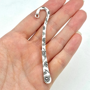 Puede incluir: Marcapáginas de plata con diseño floral. El marcapáginas tiene un gancho en la parte superior para sujetar una página.