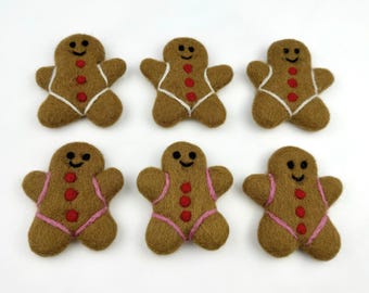 May include: Six felt gingerbread men ornaments. Three have white icing and three have pink icing. All have red buttons and smiling faces.