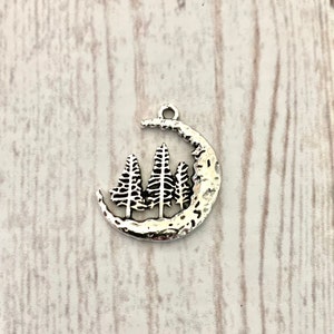 May include: Silver charm featuring a crescent moon with three stylised pine trees inside.