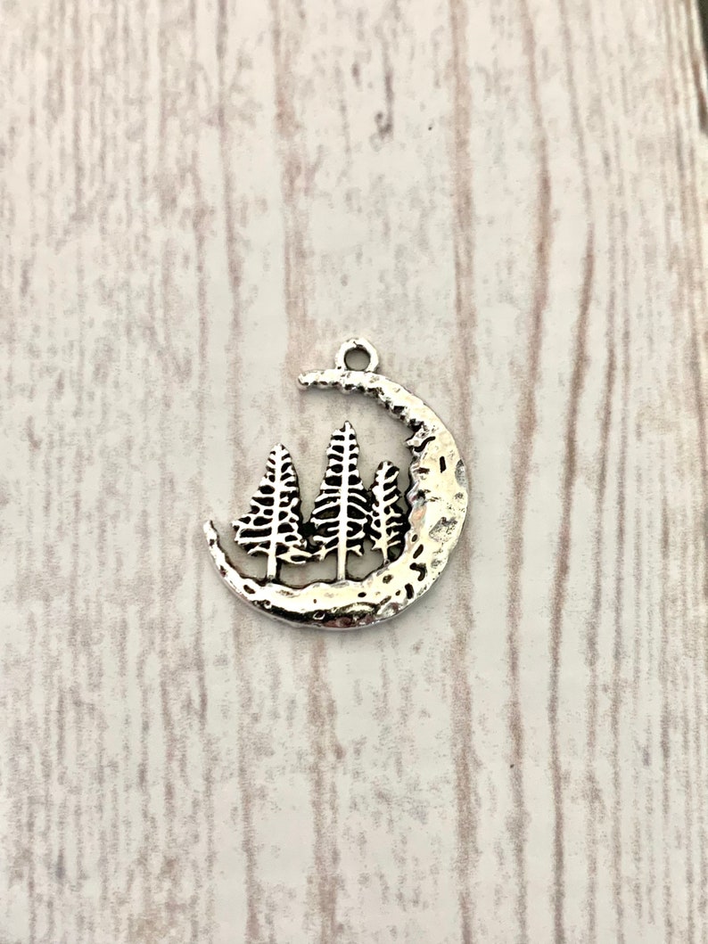 May include: Silver charm featuring a crescent moon with three stylised pine trees inside.