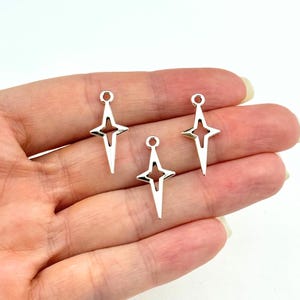 May include: Three silver star-shaped charms with a hole at the top for attaching to jewelry or other crafts.