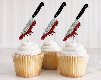 Può includere: Tre cupcake sormontati da decorazioni a forma di coltello con glitter rossi e argentati. I cupcake sono glassati con glassa bianca.