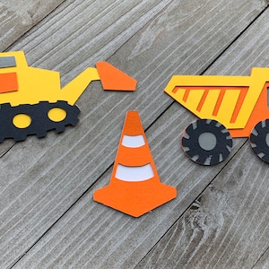 May include: Three construction-themed paper cutouts: a yellow bulldozer with a black track, a yellow dump truck with black tires, and an orange traffic cone with white stripes.
