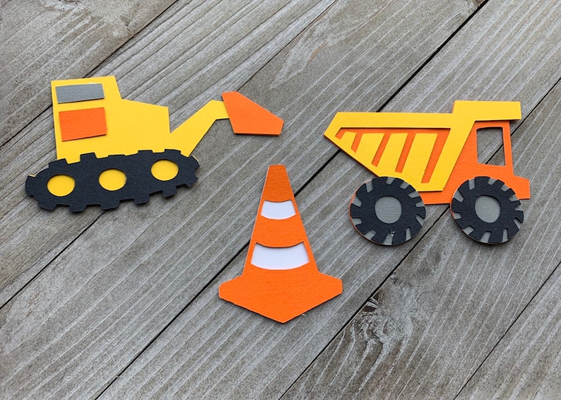 May include: Three construction-themed paper cutouts: a yellow bulldozer with a black track, a yellow dump truck with black tires, and an orange traffic cone with white stripes.