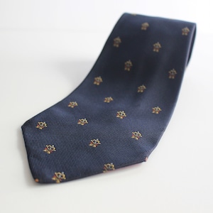 May include: A dark blue silk tie with a repeating pattern of small, gold and red geometric shapes.