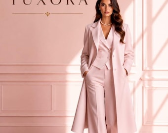 May include: A light pink three-piece suit consisting of a long coat, a buttoned vest, and wide-leg trousers. The ensemble is presented against a matching pink wall with the text TUXORA displayed in dark brown lettering above the suit.
