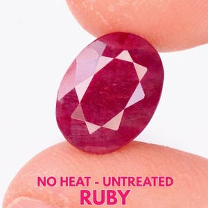 May include: An oval-cut ruby gemstone with a deep red colour and faceted surface. The stone is displayed with text printed in pink at the bottom that reads NO HEAT - UNTREATED RUBY. The gemstone features a clear, polished appearance.