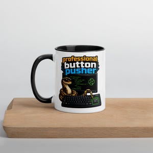 May include: A white ceramic mug with a black interior and handle. The mug features the text "professional button pusher" above a graphic of a snake coiled around a keyboard and computer screen. The design includes a Python logo.