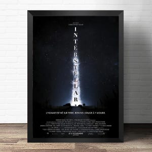 May include: A framed movie poster for Interstellar featuring a vertical beam of light against a dark, starry night sky. The title is written in white capital letters vertically. Below the light, a silhouette of a vehicle and two figures are visible.