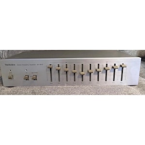 May include: A silver Technics Stereo Frequency Equalizer SH-8010 featuring a black top panel. The front face includes a power switch, two toggle switches, and ten vertical sliders for frequency adjustment, all labeled with frequency markings.