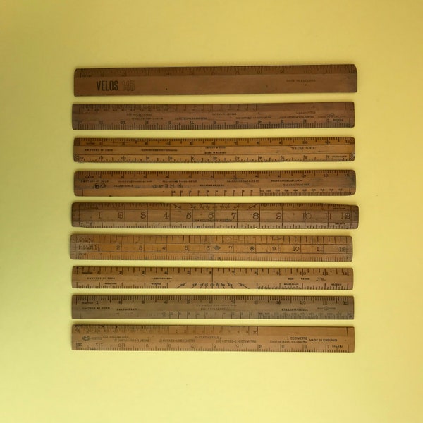 A collection of 12 inch vintage wooden rulers, including Velos 145 ruler with metal cutting edge, and mix of ages from 1920s/30s to 1960s.