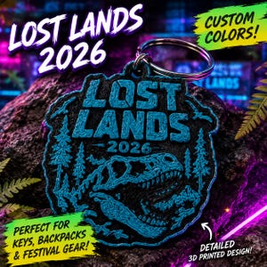 Może przedstawiać: Czarno-niebieski brelok wydrukowany w technologii 3D z napisem LOST LANDS 2026, czaszką dinozaura i sosnami. Okrągły wzór posiada metalowe kółko u góry, umożliwiające przypięcie do kluczy, plecaków lub innych przedmiotów osobistych.