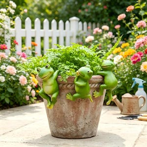 May include: A weathered terracotta-coloured plant pot featuring three green frog figurines clinging to the rim. The pot contains a lush green plant and is designed with a rope-like texture around the upper edge, providing a decorative accent.