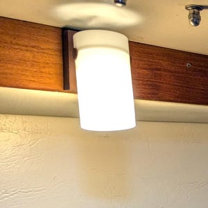 May include: Interior shot showing ceiling lights and track lighting fixtures. The lights are mounted on a dark wood beam. A painting of a beach scene is visible below the lights. The walls are painted a light beige colour.