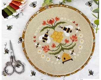 May include: A cross-stitch embroidery hoop with a bee-themed design. The design features a yellow honeycomb, red flowers, green leaves, and white daisies. There are several bees flying around the honeycomb and flowers. The hoop is surrounded by a brown fabric.