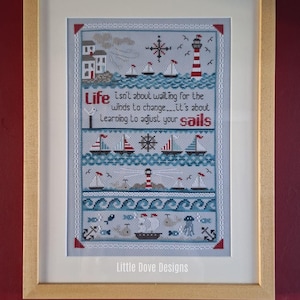 May include: Framed cross-stitch art with a nautical theme. The design features sailboats, a lighthouse, and the text "Life isn't about waiting for the winds to change...it's about Learning to adjust your sails." The frame is light brown.