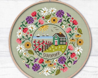 Könnte beinhalten: Eine Kreuzstichstickerei in einem Holzrahmen mit einer sommerlichen Szene aus einem grünen Haus, Segelbooten und einer Sonne, umgeben von einem kreisförmigen Kranz aus bunten Blumen wie Gänseblümchen, Sonnenblumen und Rosen, mit dem Text SUMMER.