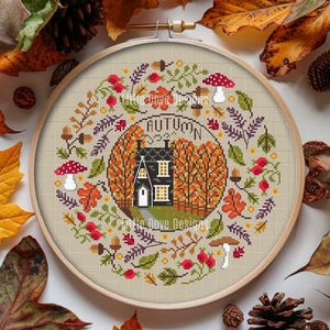 Könnte beinhalten: Kreuzstich-Stickerei in einem Holzrahmen mit einer Herbstszene. Das Design umfasst ein schwarzes Haus, Herbstlaub, Pilze und das Wort "AUTUMN". Die Farbpalette umfasst Orange, Rot, Grün und Braun.