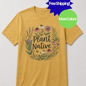 May include: A mustard yellow short-sleeve t-shirt featuring a circular botanical illustration of various wildflowers and greenery surrounding the black text Plant Native centered on the chest. The design includes purple, pink, white, and yellow flowers.