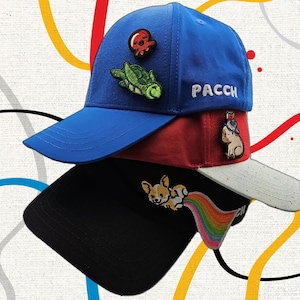 May include: A stack of three baseball caps in blue, red, and black. The blue cap features a red octopus patch, a green turtle patch, and the white text PACCH. The red cap has a light-coloured brim and a dog patch. The black cap features a corgi patch with a rainbow.