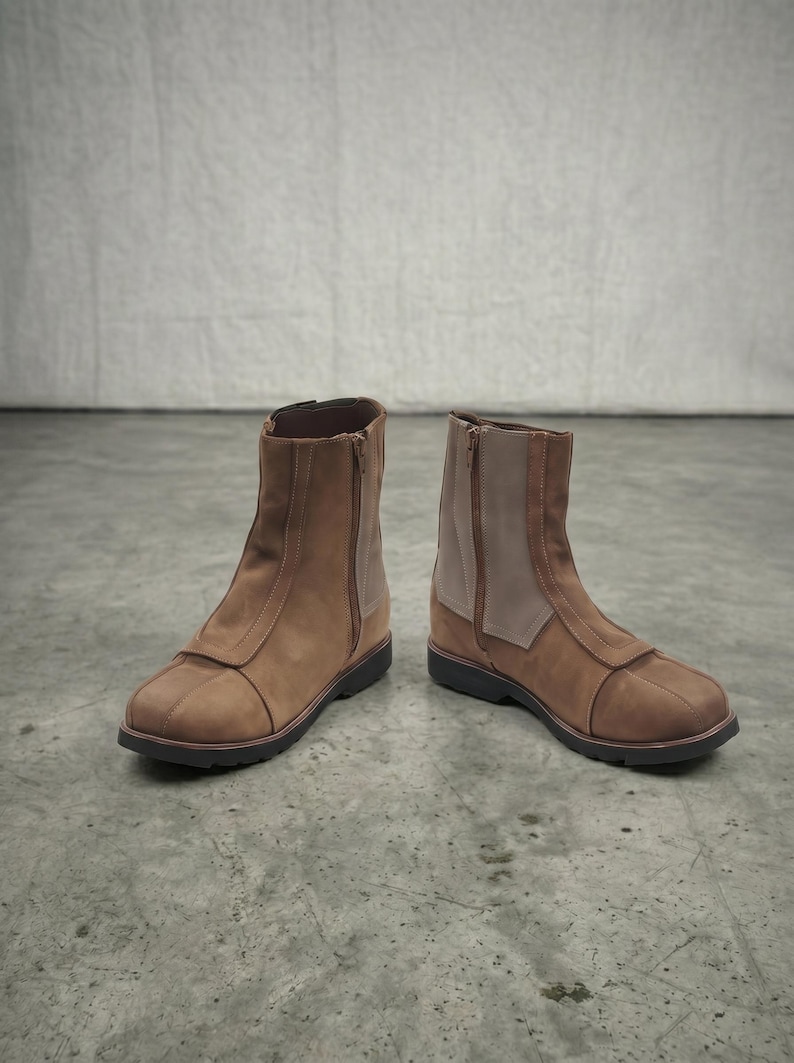 May include: A pair of brown ankle boots with a side zipper and a contrasting light brown panel. The boots have a rounded toe and a dark sole. The boots are made of a suede-like material.