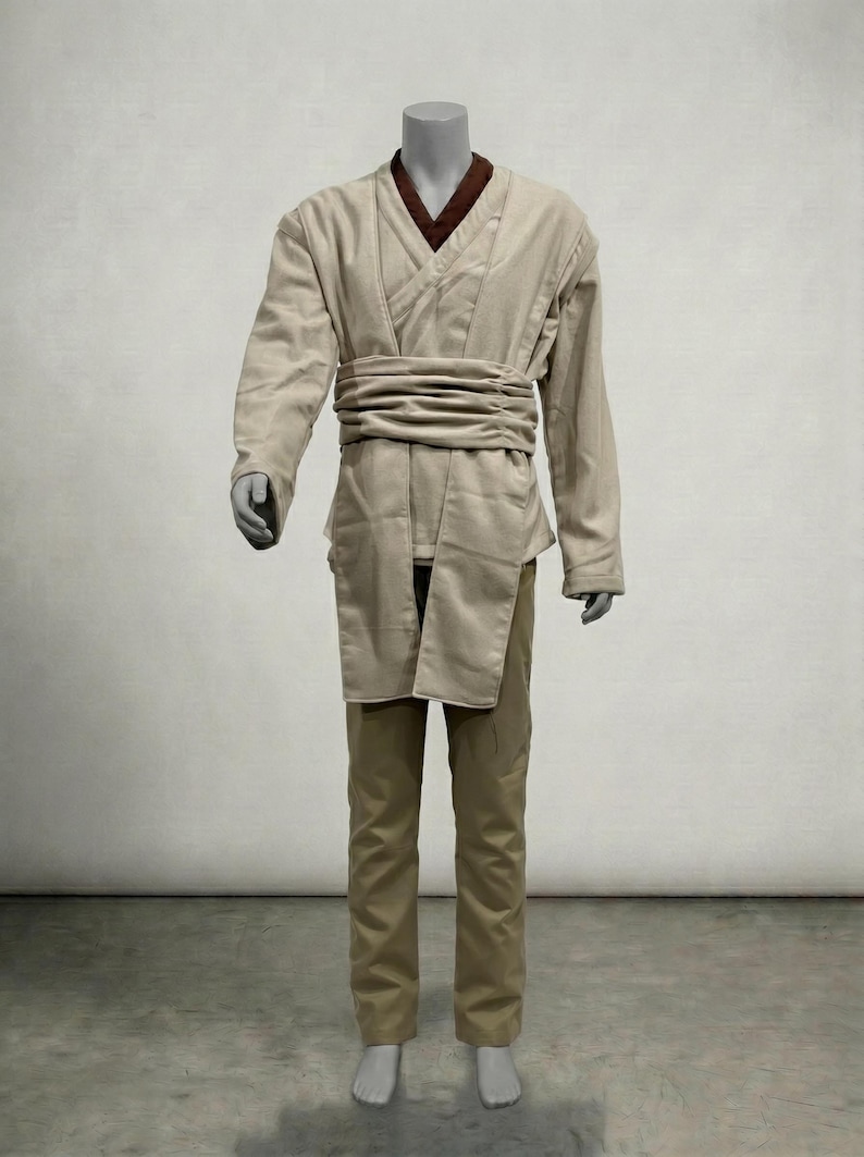 Puede incluir: Un disfraz de color beige compuesto por una t&uacute;nica de manga larga, pantalones y un cintur&oacute;n ancho. La t&uacute;nica tiene un cuello marr&oacute;n y un dise&ntilde;o envolvente. Los pantalones son de color beige a juego. El disfraz se exhibe en un maniqu&iacute;.
