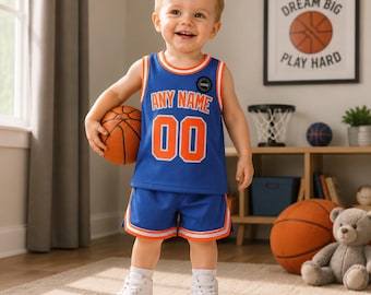 May include: A blue basketball jersey and shorts set with orange and white trim. The jersey features the text ANY NAME in orange letters above the number 00 in orange with a white outline. The set is worn with white trainers and a basketball.