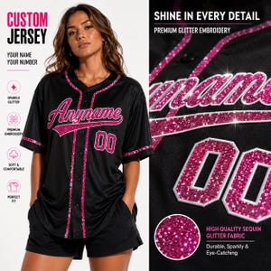 May include: A black baseball jersey featuring pink glitter embroidery that spells out Anyname and the number 00. The jersey has a button-down front with pink glitter trim along the collar, placket, and sleeve cuffs, and a matching black short.
