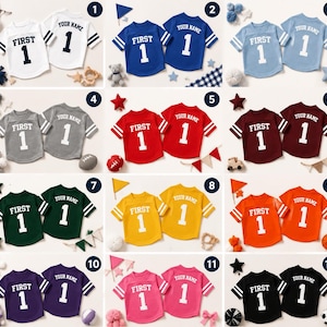 May include: A collection of twelve pairs of short-sleeved jerseys in various colours, each featuring the text "FIRST" and the number "1" on the front, with "YOUR NAME" and the number "1" printed on the back, all with striped sleeve details.